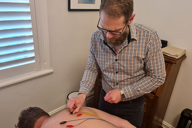 Chris Booth performing electro acupuncture treatment on a patient